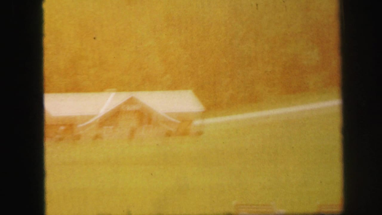 Warm overexposed view of a small building in a grassy field with dark film edges.