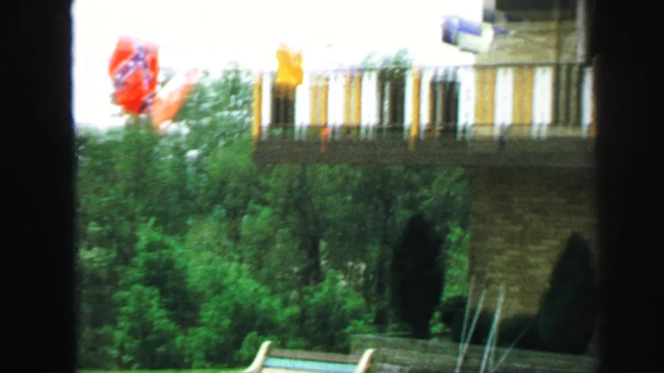 The frame shows a striped balcony, flags, shrubs, and patio furniture outside a residence in 1971 Lynbrook footage.