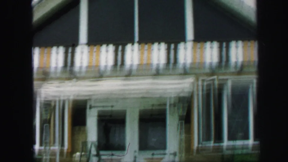 1971 Lynbrook frame with soft motion blur on striped balcony railings, entry doors, side windows, awning-like trim, and the yellow-brown exterior.