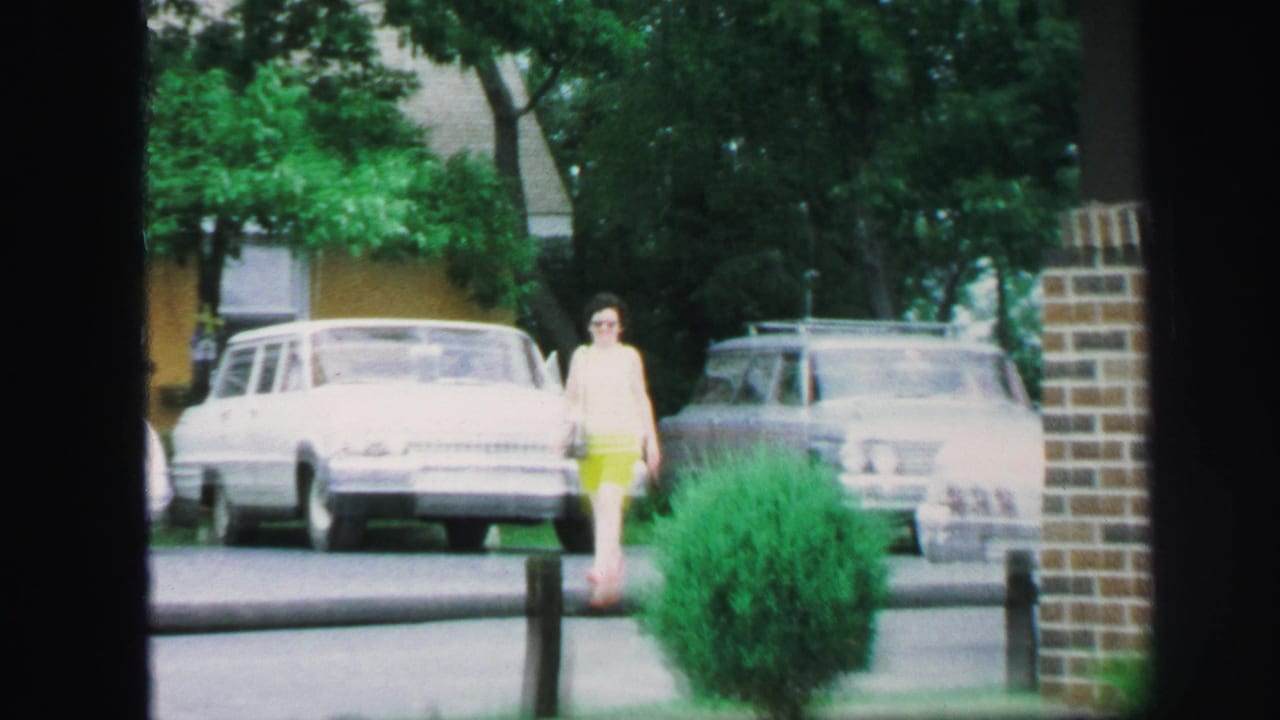 Young woman in bright shorts walks along a suburban street near parked cars and trees.