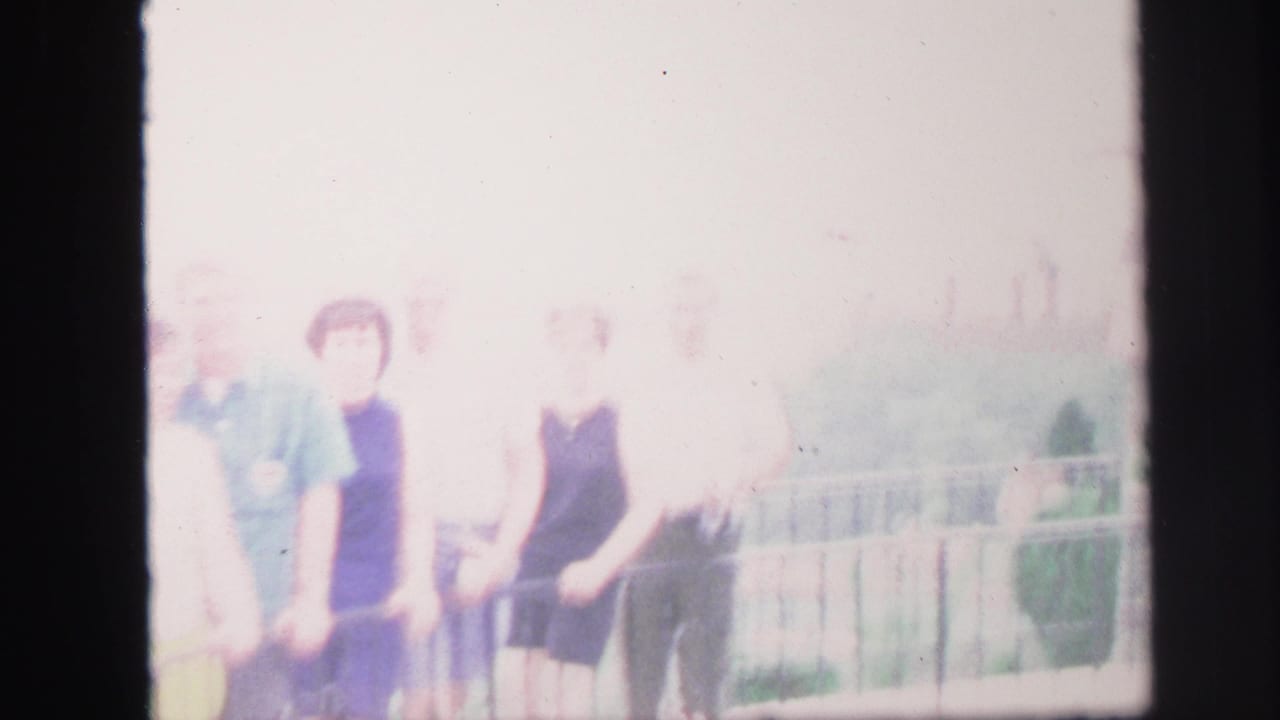 Heavily overexposed 1971 8mm frame of adults posing by a railing in Lynbrook, New York.