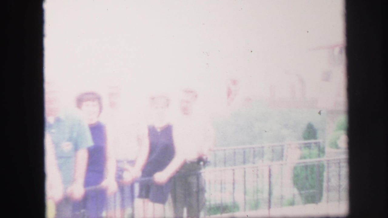 Overexposed Lynbrook home-movie frame showing adults gathered at a railing in summer clothing.