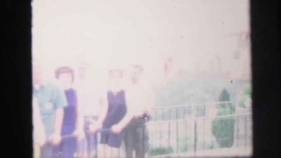 Overexposed Lynbrook home-movie frame showing adults gathered at a railing in summer clothing.