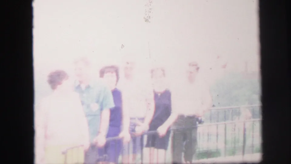 1971 8mm home-movie frame of several adults near a railing, softened by glare and motion blur.