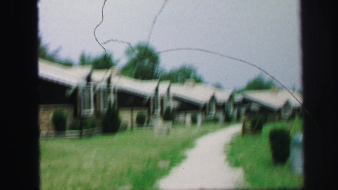 1971 8mm frame from Lynbrook, New York showing low cabins beside a pale path and green lawn.