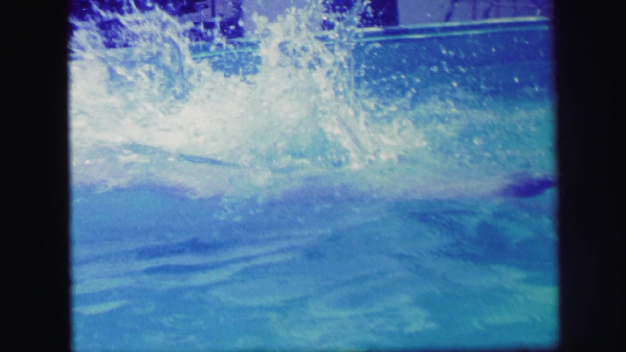 1971 Lynbrook home-movie frame showing a large splash in blue pool water after a dive or jump.