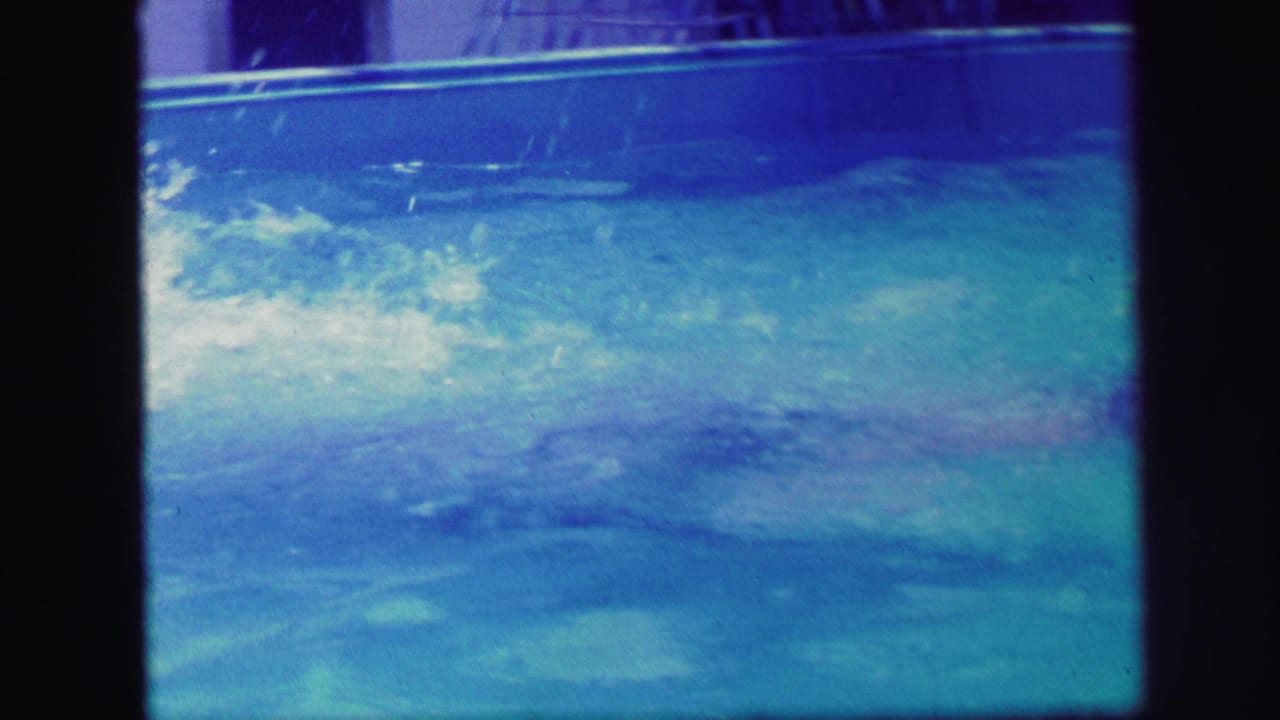 Swimmer moving underwater in a blue pool with ripples at the surface.