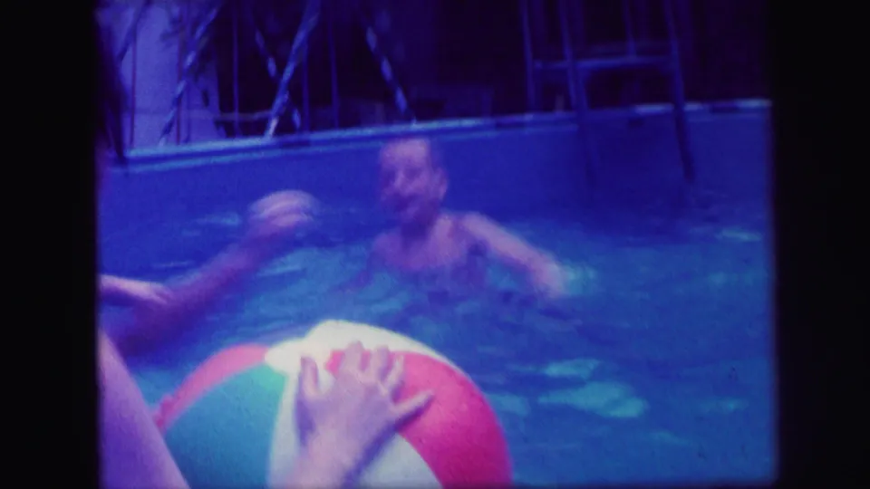 1971 Lynbrook pool scene with visible adults playing near a red, white, and green beach ball in blue-purple home-movie footage.
