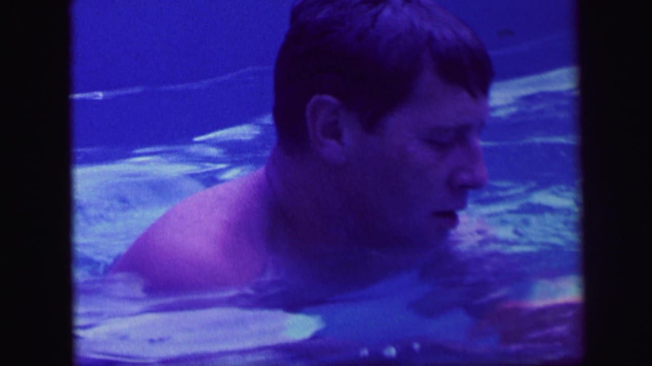 Adult man swims in blue pool water in this 1971 Lynbrook, New York 8mm home-movie frame.