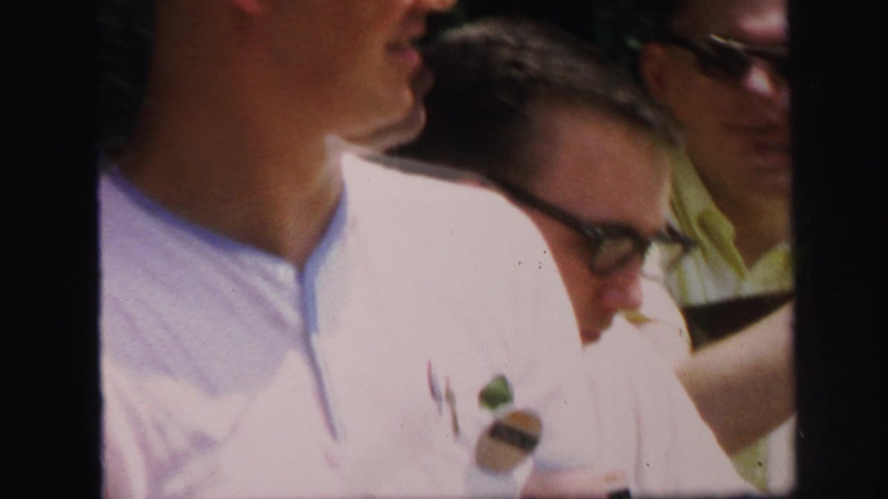 1971 Lynbrook home-movie frame showing adults gathered near a wooded target-practice shelter, with faces and eyeglasses visible.