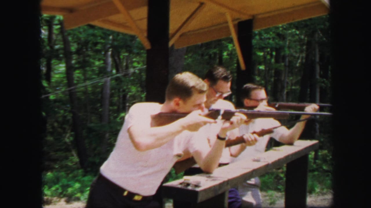Three adult men in white shirts aim rifles from a wooden shooting bench in 1971 Lynbrook, New York home-movie footage.