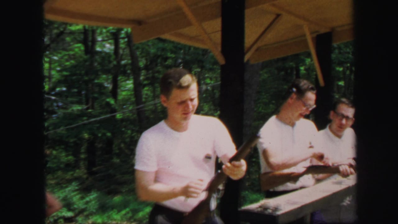 One young man holds a rifle while two others handle rifles at the bench.