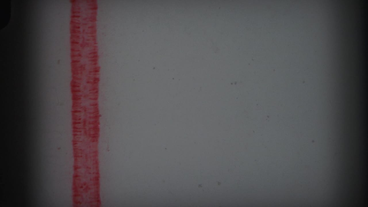Red vertical marker line on pale film stock with dark edge vignette and dust specks.