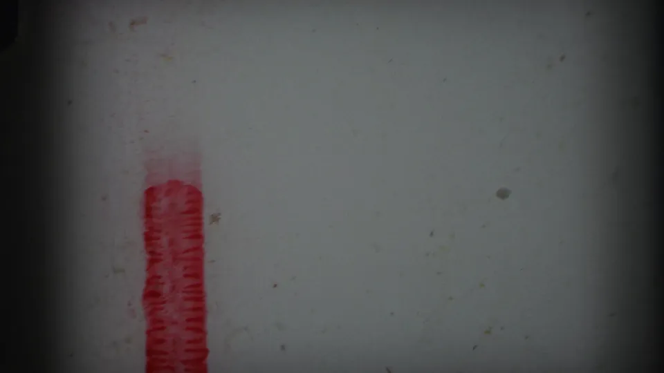 1971 Lynbrook 8mm frame with a short red marker segment near the lower left, pale film stock, dust specks, grain, and dark edge falloff.