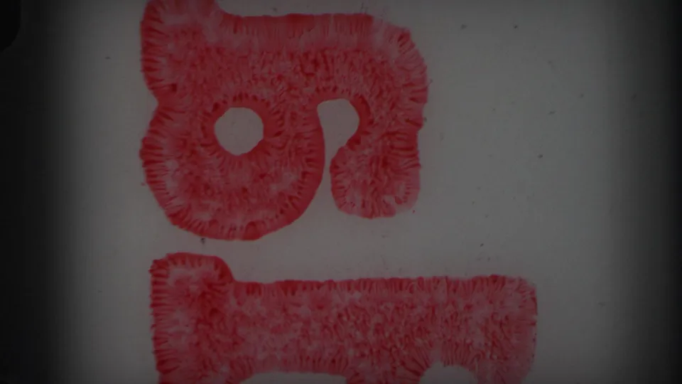 1971 8mm Lynbrook reel frame with red looped markings on blank film, including a rough W-like form, grain, dust, and gate shadows.
