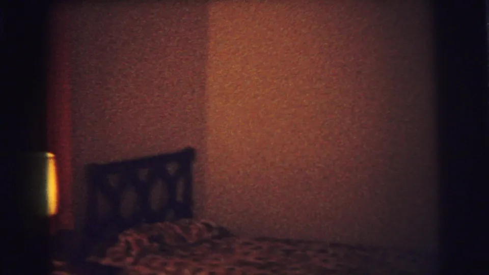 1973 Lynbrook bedroom view with patterned bedding, a dark headboard, textured wall surface, and a shadowed central doorway or furniture edge.
