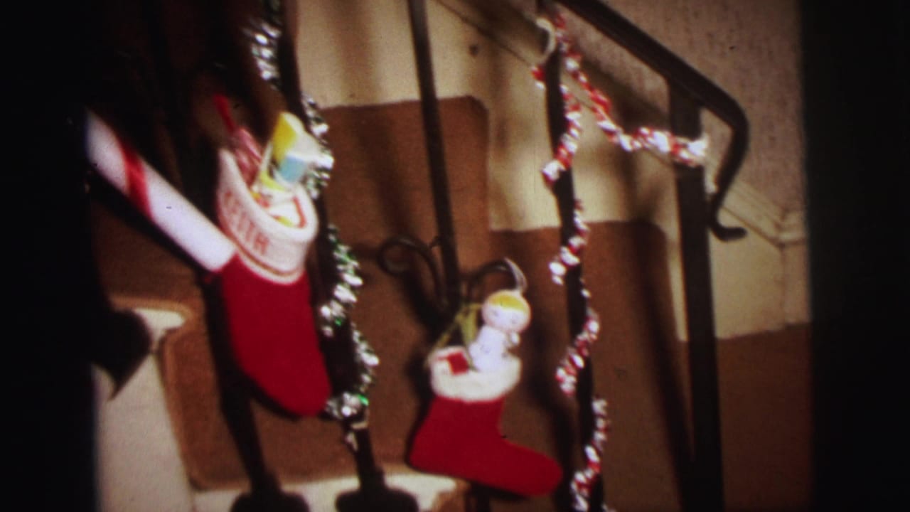 1973 Lynbrook home-movie frame showing red stockings, tinsel, and a candy-cane decoration on an indoor stair rail.