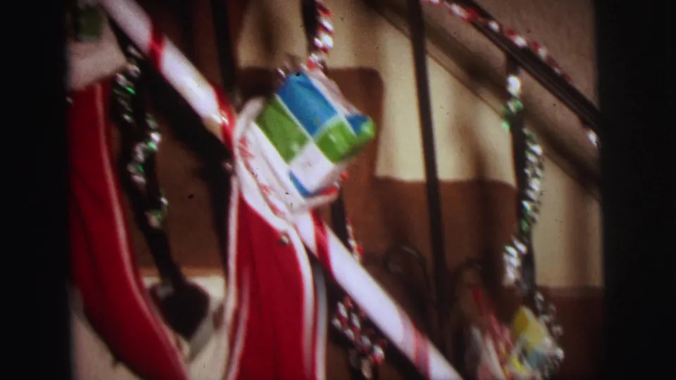 Close 8mm view of Lynbrook Christmas stair decorations, with a red stocking, candy cane, tinsel, and small gift boxes.