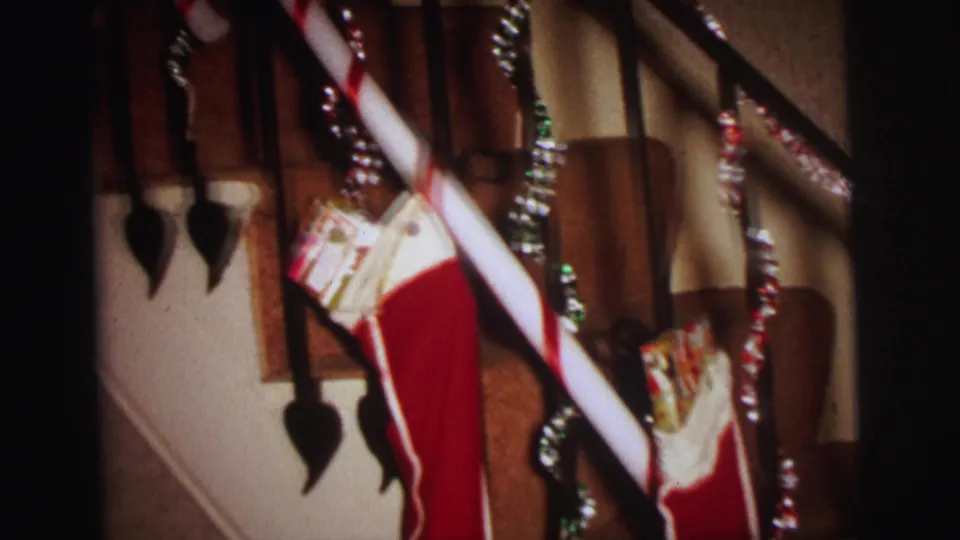 Lynbrook Christmas staircase detail with a red stocking, visible gifts, tinsel strands, dark spindles, and striped stair carpet.