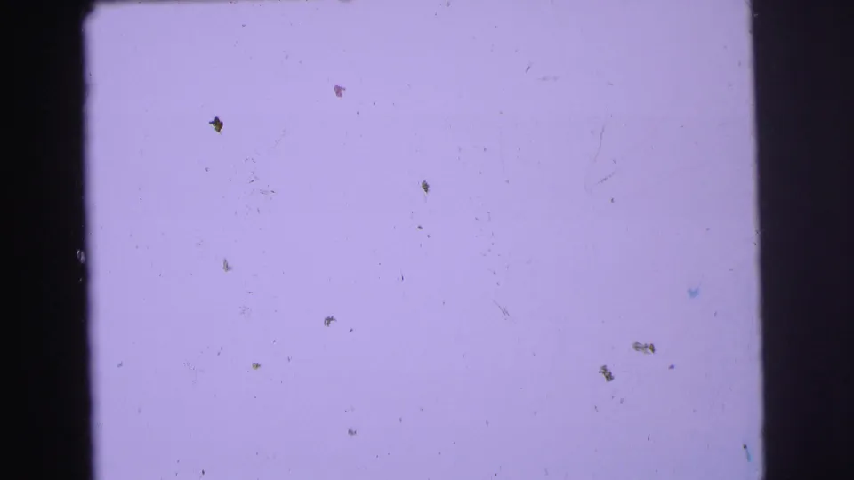 Soft, mostly blank 1973 8mm frame from the Lynbrook reel with pale purple exposure, dust, scratches, and gate-edge shadow.