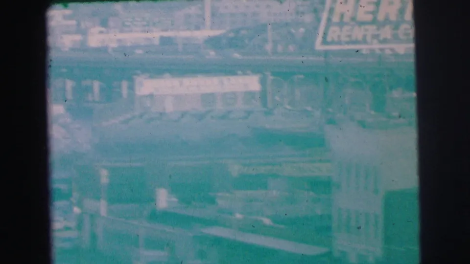 1973 Lynbrook 8mm view from above, showing Hertz signage near storefronts and a horizontal bridge or roadway edge.