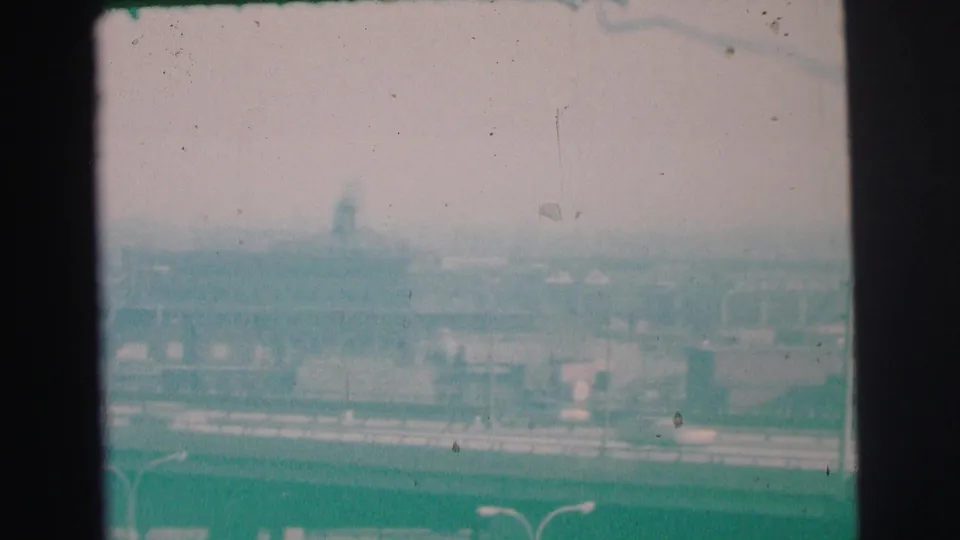 1973 Lynbrook 8mm frame looking across low buildings, vehicles, haze, and a distant water tower-like form.