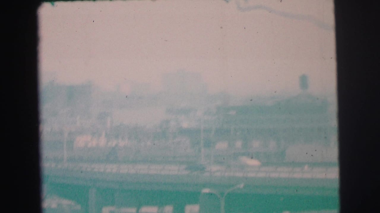 Soft, hazy roadway view with distant buildings and a tower shape under an overcast sky.