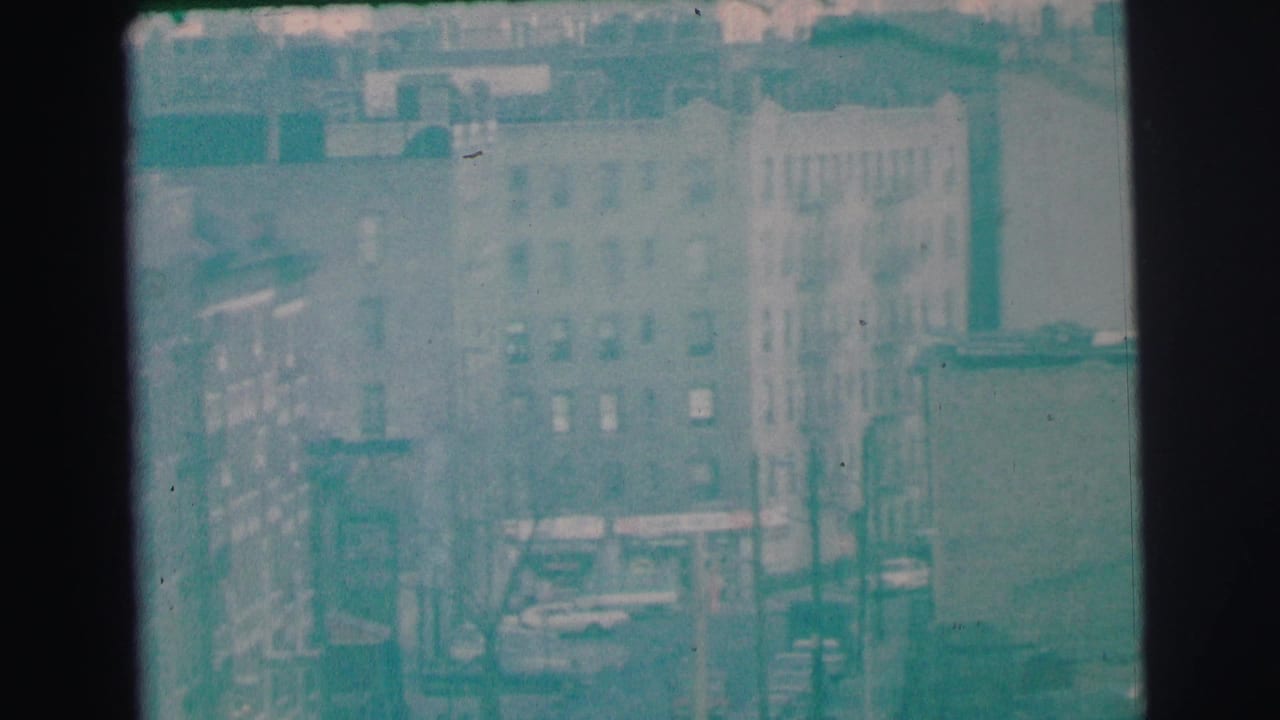 1973 Lynbrook, New York frame showing multi-story masonry buildings, windows, a street, and faint storefront signage.
