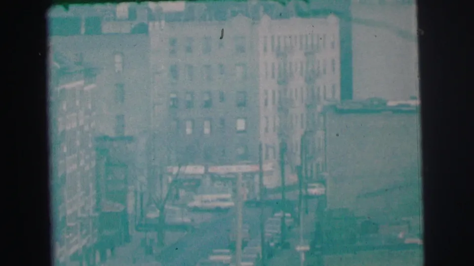 1973 Lynbrook, New York street view with apartment-like buildings, parked cars, windows, and indistinct commercial signage.