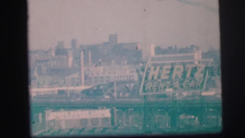 1973 Lynbrook home-movie frame showing the Hertz Rent-A-Car sign partly softened by grain, haze, and green-tinted exposure.