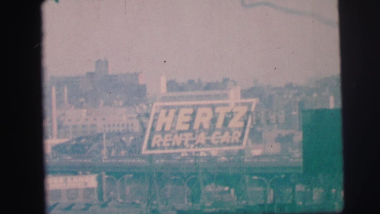 1973 Lynbrook, New York 8mm frame showing a large Hertz Rent-A-Car sign against a hazy industrial skyline.