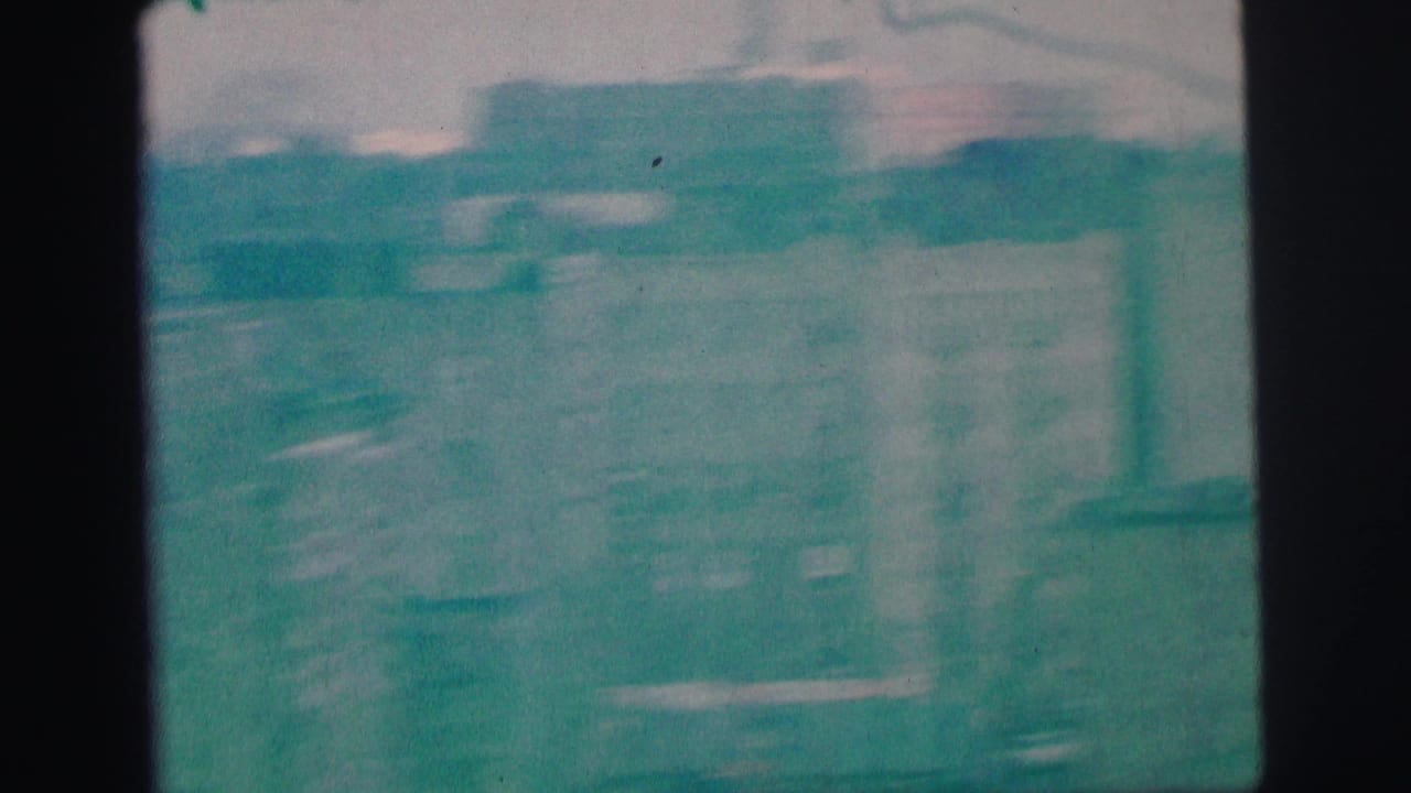 Soft, teal-tinted elevated view of buildings and street shapes through aged 8mm film.