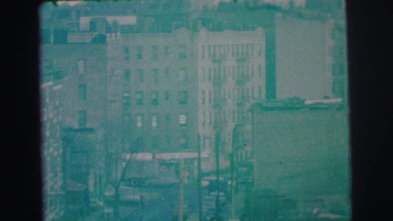 Lynbrook, New York street scene in 1973 with brick apartment buildings, fire escapes, traffic, and a rent-a-car sign area noted by metadata.