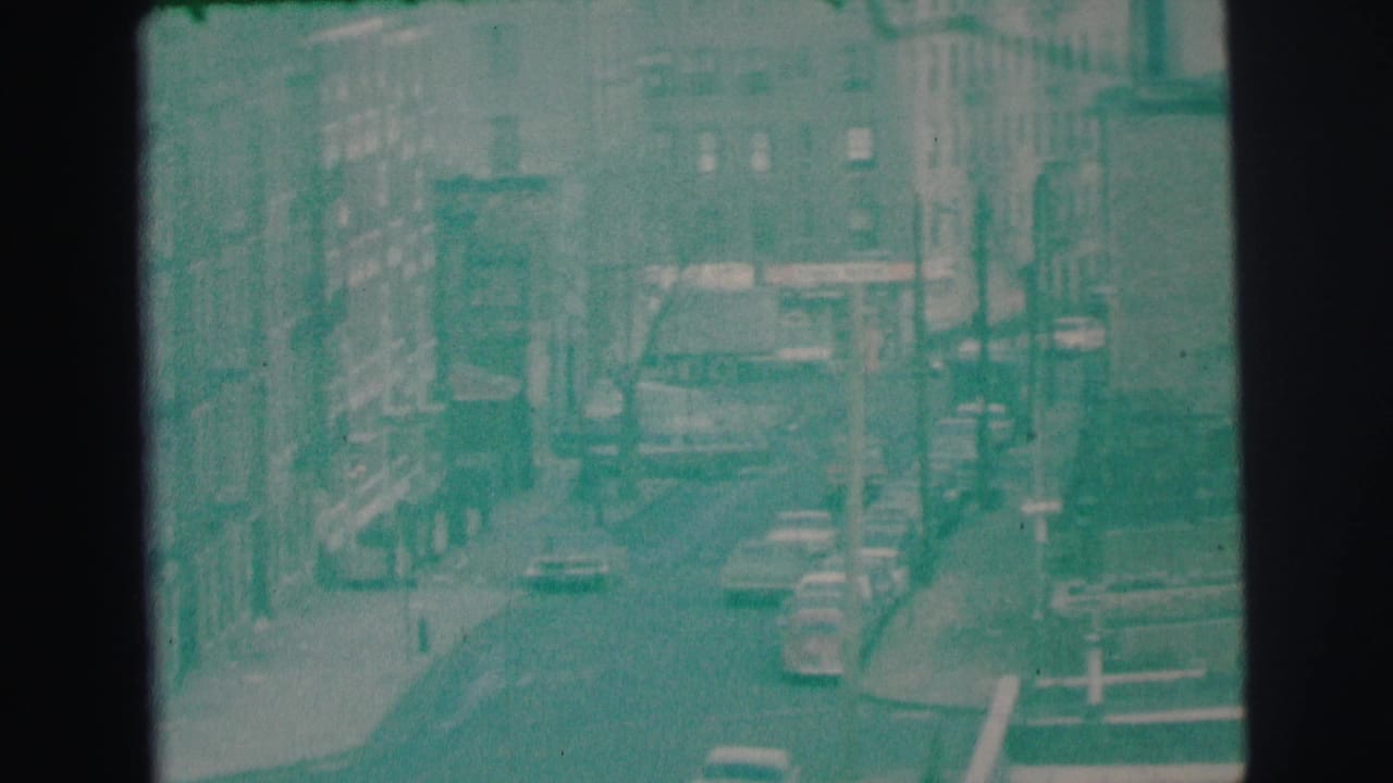 1973 Lynbrook, New York 8mm frame looking down over a street lined with buildings, cars, and utility poles.