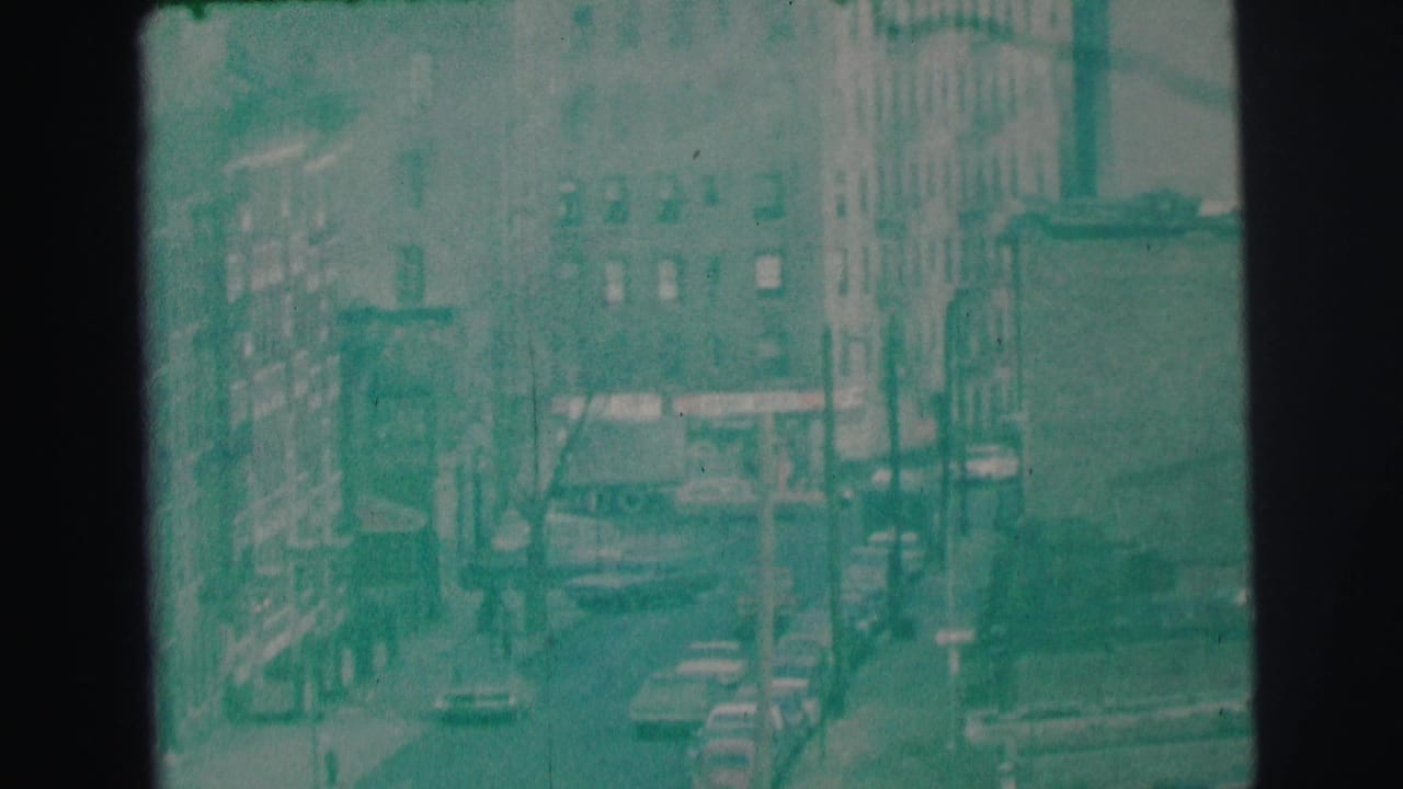 Soft high-angle view of a city street with cars, buildings, poles, and a dark frame edge.