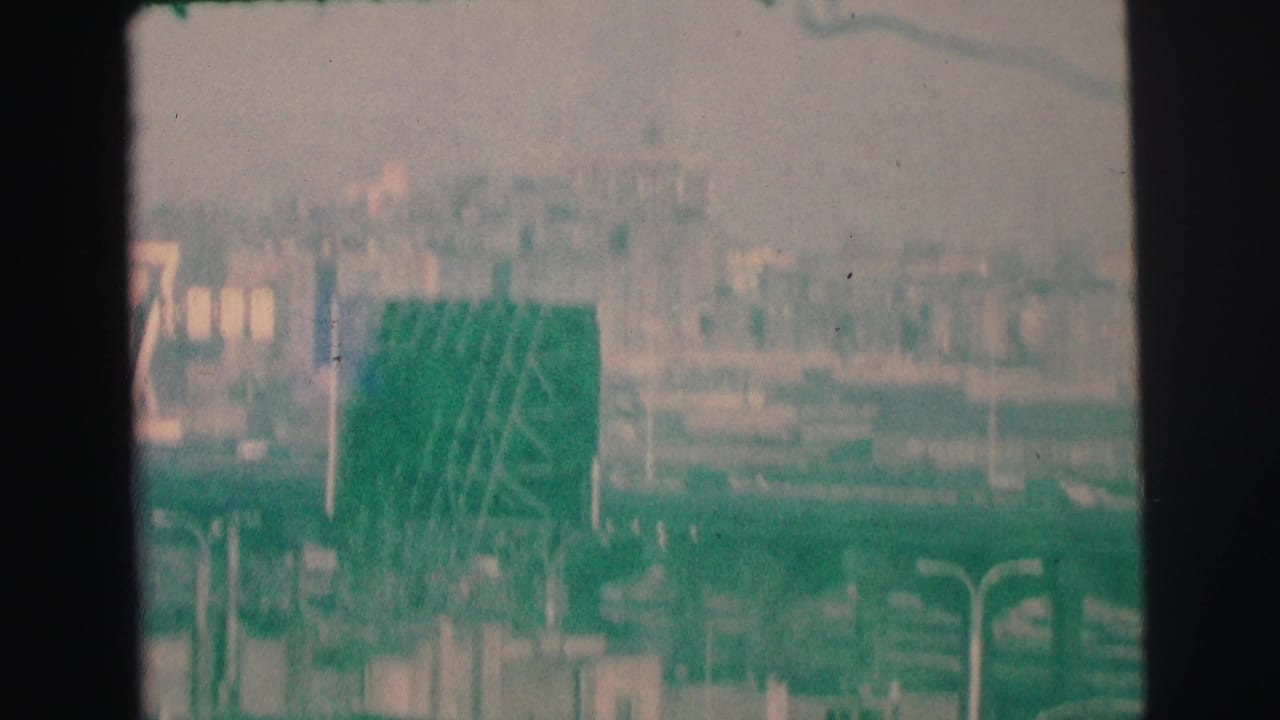 Hazy elevated view with a green roadside sign and distant low-rise buildings.