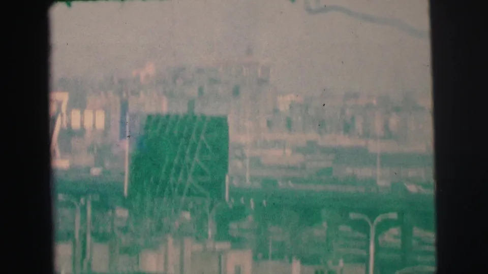 1973 Lynbrook, New York 8mm frame showing a hazy elevated view across roads, poles, signage, and distant buildings.