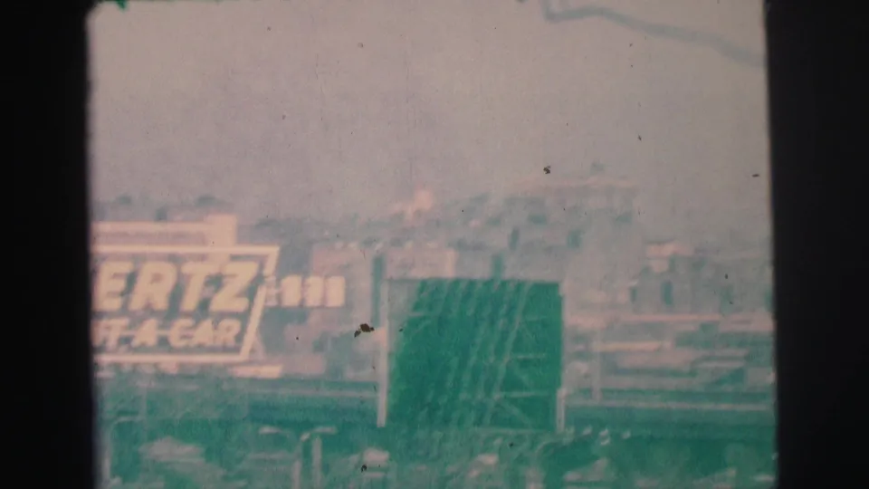 1973 Lynbrook, New York frame with a visible Hertz sign, roadside signage, poles, and hazy commercial buildings beyond.