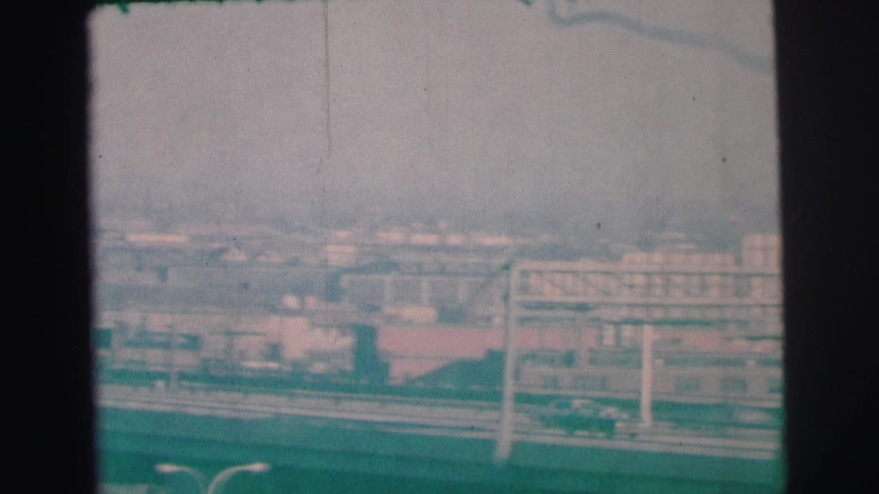 Hazy elevated view over a roadway with cars, railings, rooftops, and distant buildings.