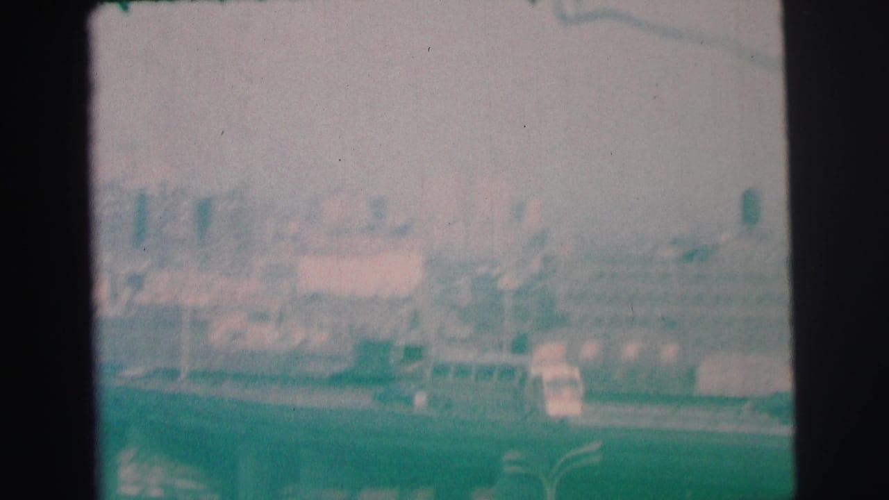 Distant roadway scene with vehicles, low buildings, haze, and indistinct taller structures.
