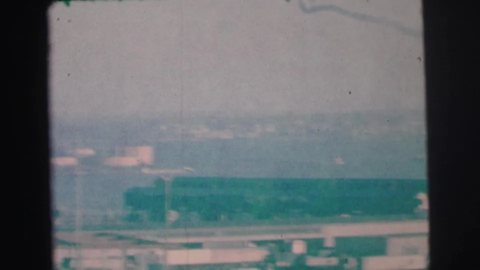 1973 Lynbrook, New York home-movie frame looking over rooftops and roadway edges toward a hazy distant landscape.