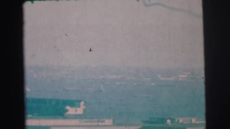 1973 Lynbrook, New York frame showing a hazy low landscape with distant structures, a road edge, and a small bright vehicle-like form.