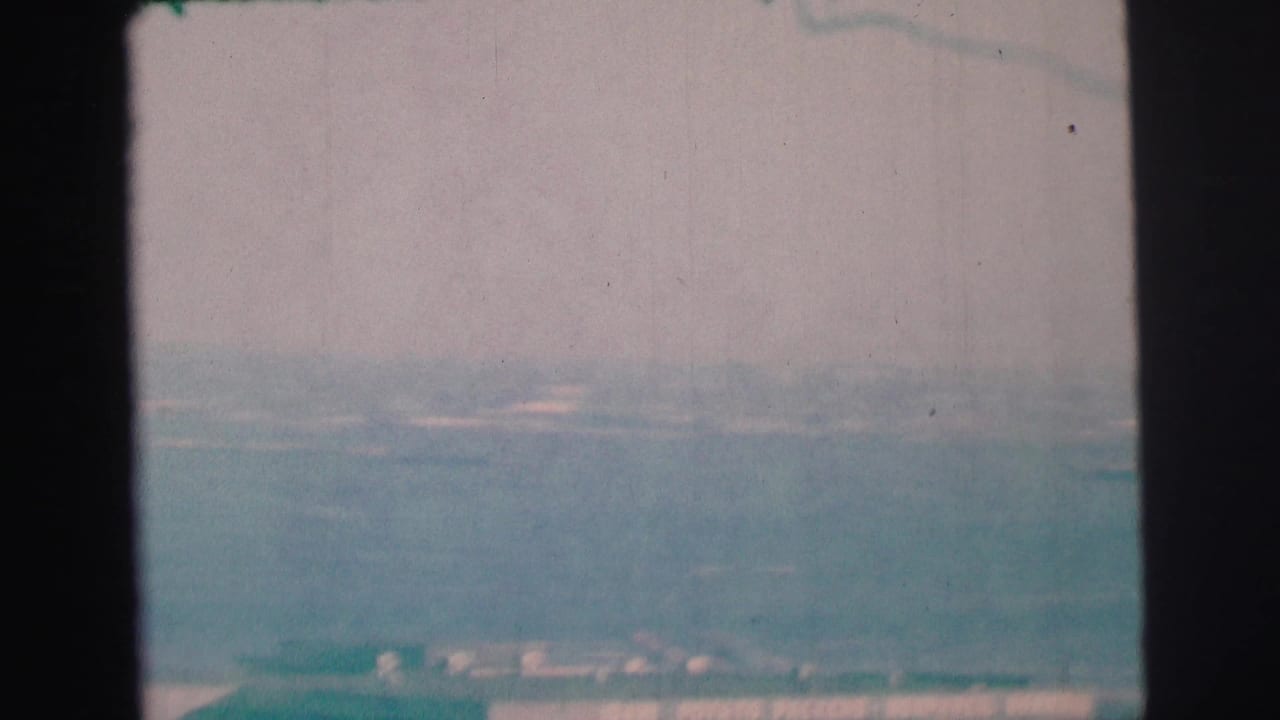 1973 8mm frame from Lynbrook-area footage showing blue-green bay water, pale sky, and a faint distant shoreline.