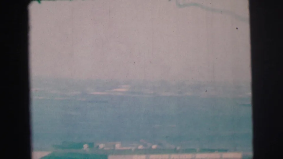 1973 8mm frame from Lynbrook-area footage showing blue-green bay water, pale sky, and a faint distant shoreline.