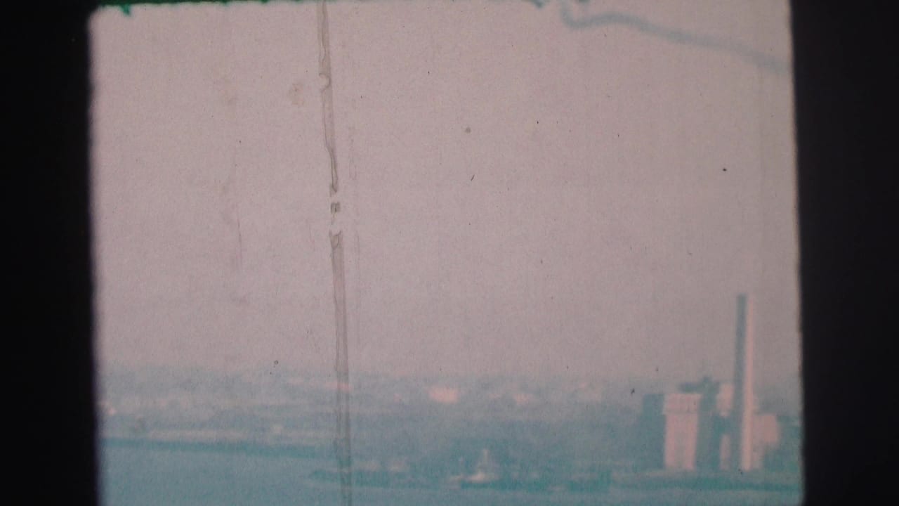 1973 Lynbrook, New York 8mm frame with industrial buildings and smokestacks emerging through haze beyond the bay.