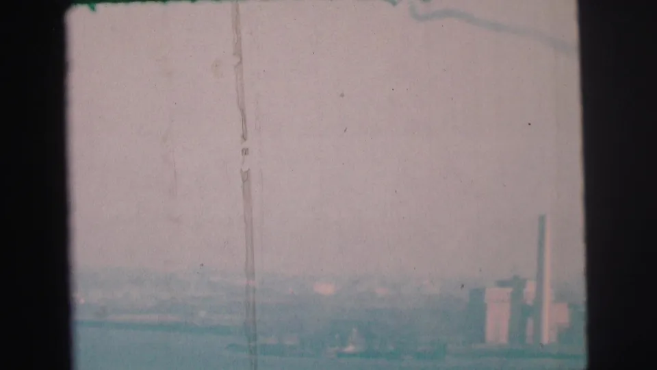 1973 Lynbrook, New York 8mm frame with industrial buildings and smokestacks emerging through haze beyond the bay.