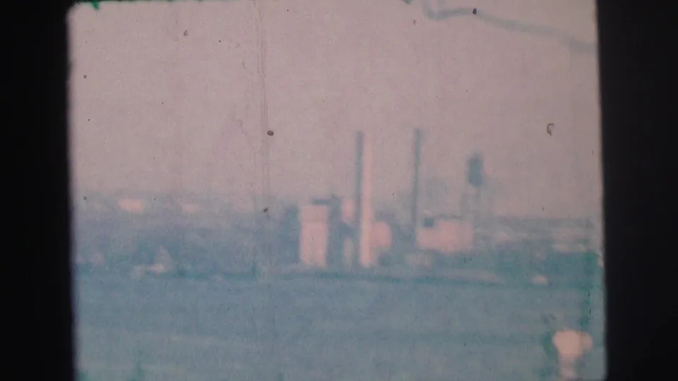 End of the 1973 Lynbrook-area 8mm pan, showing distant industrial buildings, smokestacks, haze, and bay water.