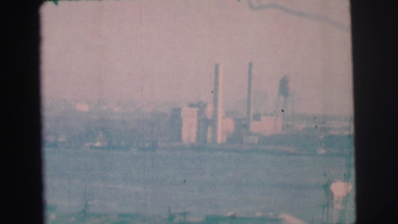 Hazy water view with smokestacks and industrial buildings beyond the shoreline.