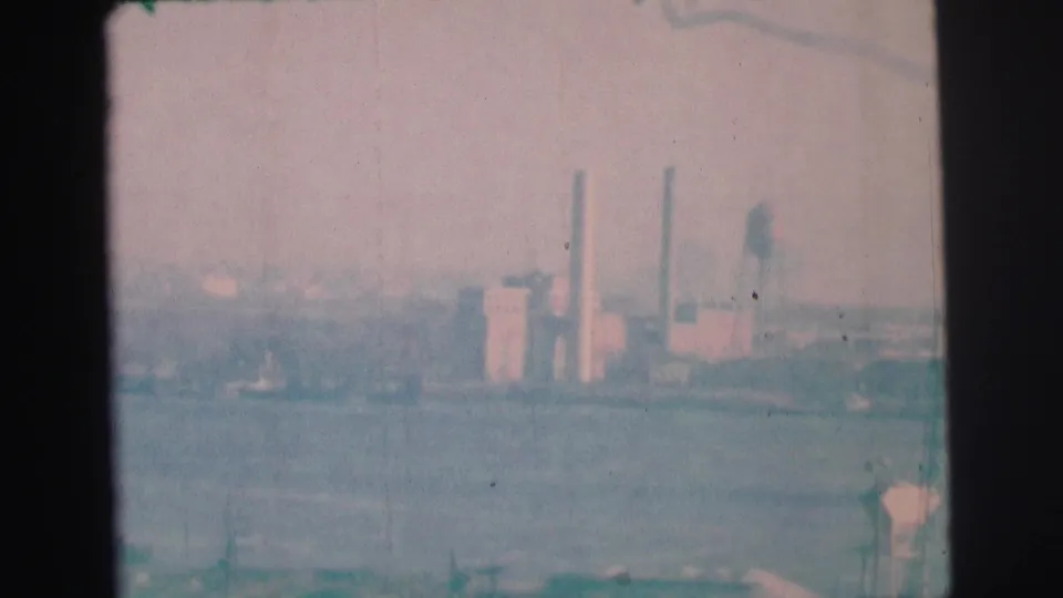 1973 Lynbrook, New York 8mm frame showing a hazy waterfront view with smokestacks, low buildings, and a pale sky.
