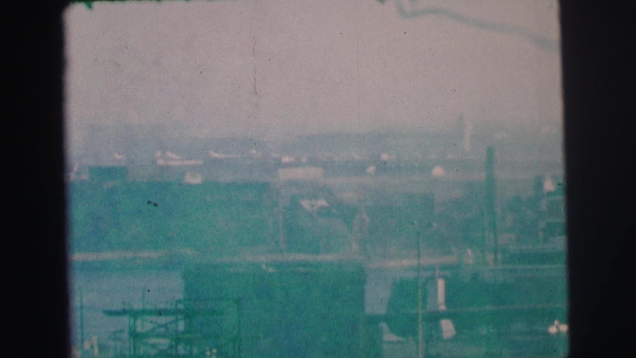 1973 Lynbrook, New York 8mm frame with a soft, blue-green view of shoreline buildings, water, and distant industrial forms.